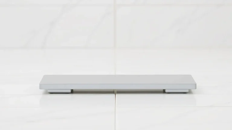 A minimalist gray bathroom scale placed on a white tiled floor.